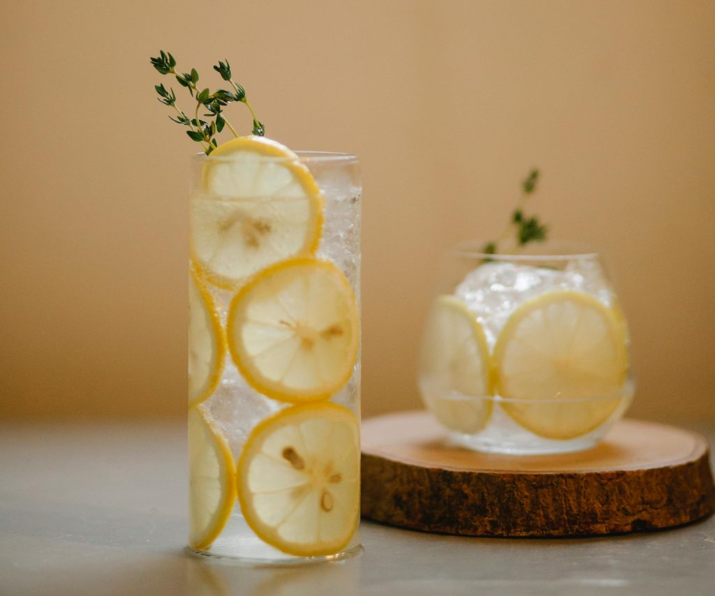 A cool, refreshing drink with lemon slices and thyme in clear glasses on a wooden coaster.
